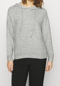 Grauer Kapuzenpullover mit weichem Material, Zugbandakzenten und langen Ärmeln. Über schwarzen Hosen getragen. Einfaches, lässiges Design.