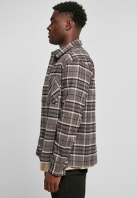 Grijze, geruite flanellen shirt met lange mouwen, knoopsluiting bij de kraag, twee borstzakken en een ruitpatroon met zwarte en crèmekleurige accenten.