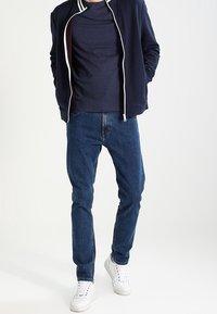 Marinblå zip-up jacka med vita ränder, marinblå t-shirt, blå jeans och vita sneakers. Avslappnad outfit med en lös passform.