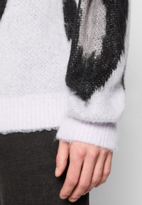 Helles lila Sweatshirt mit schwarzen und grauen abstrakten Mustern, aus weichem, flauschigem Material. Rippbündchen und Saum, die ein strukturiertes Design zeigen.