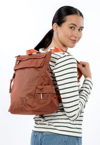 Orange tekstureret rygsæk med lynlåslukning på toppen og forlomme. Justerbare stropper, metalliske detaljer og et mønstret finish.