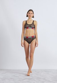 Μαύρο δαντελένιο μπραλέτ και σετ μπικίνι με κόκκινες και λευκές ελαστικές ταινίες με λογότυπο. Διαφανής υφή με λουλουδάτο σχέδιο. Απλή, αθλητική γραμμή.