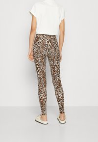 Dierlijke print leggings in tinten van bruin en goud; aangesloten ontwerp met een gladde textuur. Gekleed met een cropped wit topje en casual schoeisel.