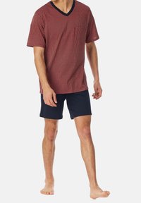 Rot gemustertes kurzärmeliges V-Ausschnitt-Shirt mit einer Brusttasche, kombiniert mit marineblauen Shorts. Der Stoff ist weich und leicht.