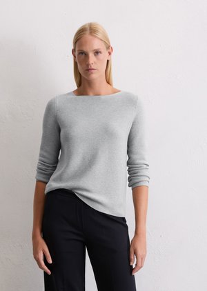 Pull en tricot gris avec un col bateau et des manches longues, doté un ourlet légèrement courbé et d'un tissu doux et texturé. Associé à un pantalon sombre.