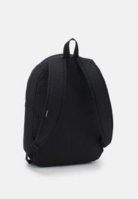 Mochila negra con correas acolchadas y contorneadas, un asa en la parte superior, tela suave y un bolsillo lateral. Diseño simple, sin logotipos visibles.