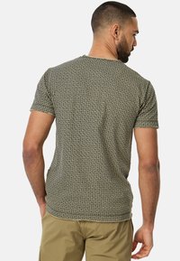 Kortærmet t-shirt i jordfarver med et geometrisk mønster. Fremstillet af blødt stof med rund halsudskæring og tætsiddende design.