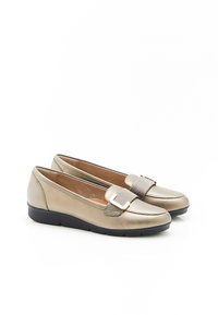 Mocassins beige métalliques avec une semelle noire plate. Présentent une sangle texturée et un accent de boucle sur le devant. Texture supérieure lisse.