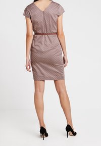 Robe marron à pois avec des manches courtes style casquette, dos en V, silhouette ajustée, taille cintrée avec une ceinture marron, associée à des escarpins noirs.