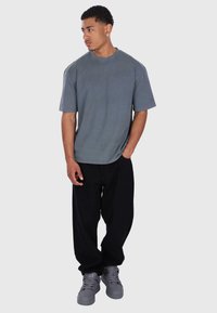 Grå bomulds t-shirt med rund hals og korte ærmer, parret med løse sorte bukser og grå højhælede sneakers. Enkel, funktionel design.