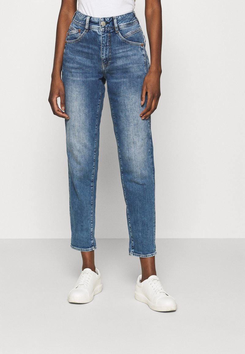 Ljusblå denimjeans med hög midja, rak ben och lätt blekning. Kombinerade med vita sneakers, utan några anmärkningsvärda mönster eller detaljer.