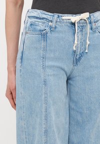 Lyseblå denimjeans med strikk i midjen, med en avslappet passform, frontlommer og synlige søm detaljer.