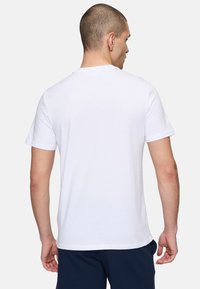 Vit bomull T-shirt med korta ärmar, rund hals och en enkel design. Bakstycket är slätt utan ytterligare detaljer eller mönster.