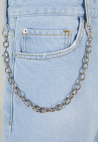 Világoskék farmeranyag, egy kis zsebbel, amelyen egy ezüst lánc található, ovális láncszemekből álló, matt fényű.