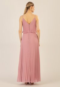 Lang, plisseret kjole i blød pink med V-udskæring og tynde stropper. Stoffet er let og flydende, med en skjult lynlås bagpå.