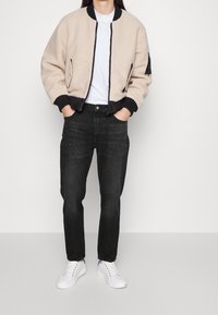 Beige sherpa bomberjacka med svarta ribbade muddar och nederkant, med dragkedja fram, kombinerad med mörka jeans och vita sneakers.