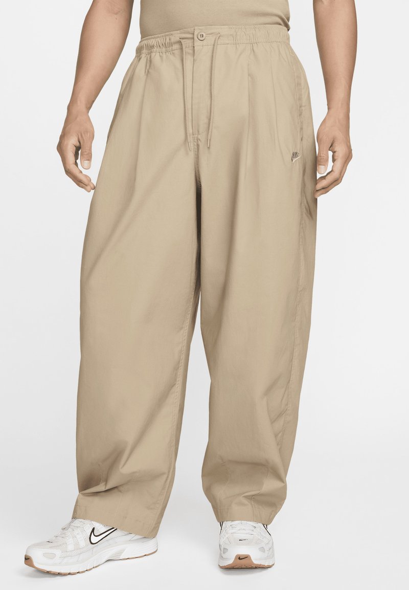 Pantalones sueltos de color beige, ligeros, con cintura elástica y cordón. Presentan un pequeño logo en la parte delantera. Tejido texturizado.