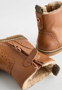 Bruine leren enkellaarsjes met een textuur, warme voering, rits aan de voorkant, decoratieve perforaties en een patroonaccent op de achterkant.
