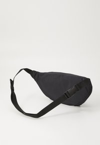 Sling bag in tessuto nero con forma triangolare, tracolla regolabile e fibbia di rilascio laterale. Texture liscia con design minimalista.