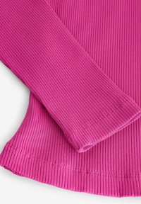 Close-up van geribbelde roze stof die de mouw en zoom laat zien met gedetailleerd stiksel op een vlakke ondergrond.