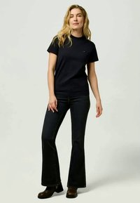Black cotton t-shirt with a crew neck, paired with dark flared jeans. Model wears brown ankle boots, presenting a relaxed casual outfit.