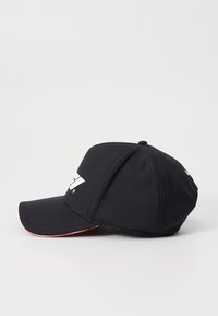 Czarna czapka bejsbolowa wykonana z teksturowanej tkaniny. Posiada zakrzywiony daszek, z białym logo z przodu oraz czerwonym akcentem wzdłuż krawędzi daszka.