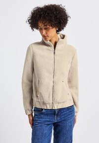 Giacca in pile beige con zip frontale, collo alto e vita elastica. Presenta tasche laterali e tessuto testurizzato per il calore.