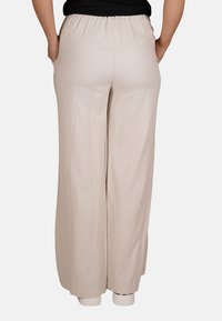 Pantaloni beige a gamba ampia con vita elastica, realizzati in tessuto leggero, caratterizzati da una texture liscia e senza motivi visibili.