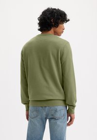 Olijfgroene sweatshirt met een ronde hals, lange mouwen en geribde manchetten. Gecombineerd met lichtblauwe jeans, wat zorgt voor een casual pasvorm en zachte textuur.