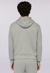 Šedá mikina s kapucí vyrobená z měkké látky. Zobrazuje zadní pohled, velkou kapuci, žebrované manžety a uvolněný střih. Žádné viditelné loga ani vzory.