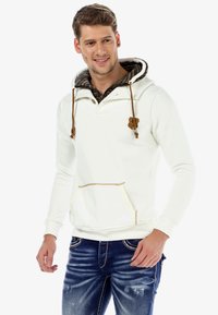 White hoodie with a patterned inner lining, drawstrings, and a kangaroo pocket. Worn with blue jeans featuring light distressing.