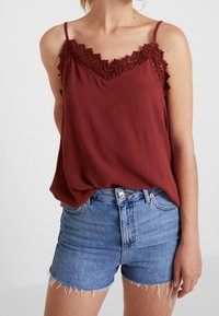 Camiseta burdeos con encaje en el escote, combinada con pantalones cortos de mezclilla azul claro con dobladillos deshilachados. Tela suave, corte relajado.