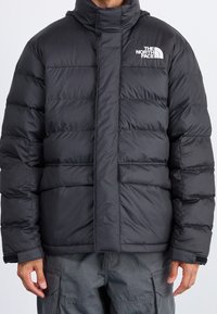 Giubbotto invernale nero con colletto alto, caratterizzato da un design a righe orizzontali, chiusura frontale con zip e logo sul lato sinistro del petto.