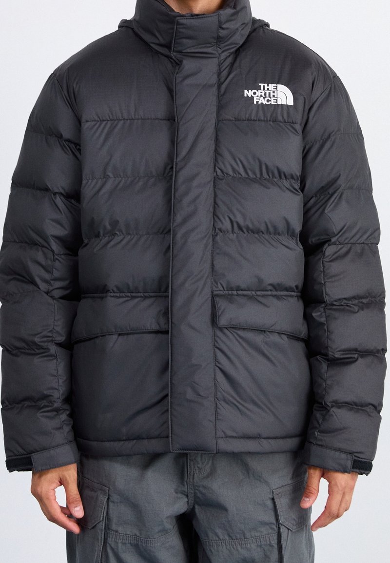Giubbotto invernale nero con colletto alto, caratterizzato da un design a righe orizzontali, chiusura frontale con zip e logo sul lato sinistro del petto.