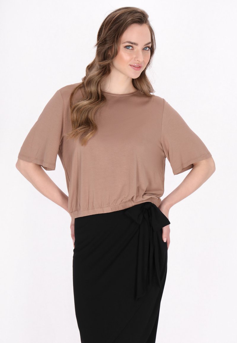 Bruin kort mouwloos crop top met een losse pasvorm, gecombineerd met een zwarte wikkelrok met een zijstrikaccent en een zachte textuur.