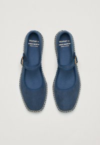 Zapatos Mary Jane de ante azul con puntera redonda, un acento de hebilla y detalle de costura beige alrededor de la suela. Hechos en España.