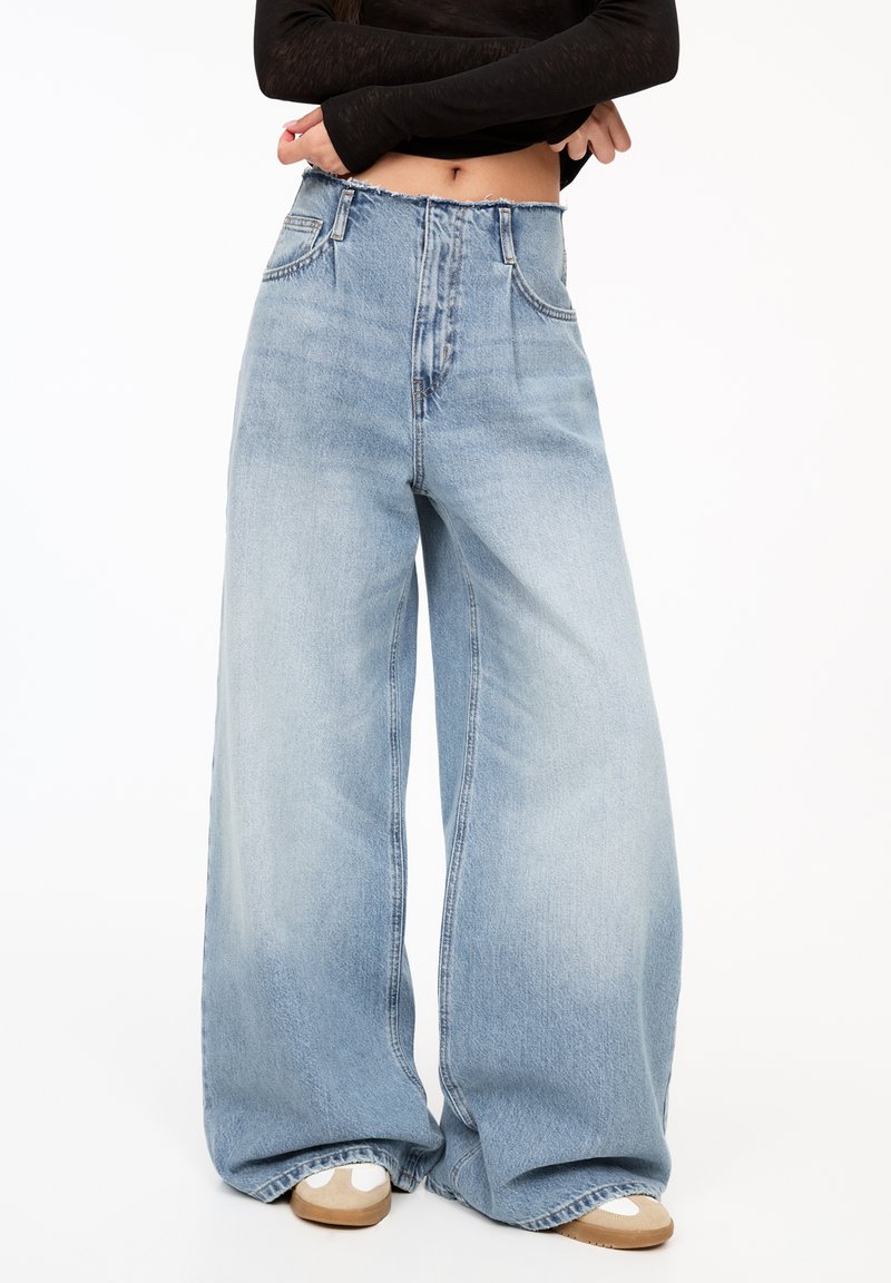 Jeans a gamba larga di colore blu chiaro con vita alta, orlo superiore sfilacciato e due tasche frontali. Realizzati in denim con una finitura morbida e texturizzata.
