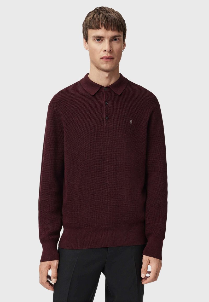 Burgundy sweater with a ribbed texture, long sleeves, and a polo collar. Features three buttons and a small emblem on the chest.