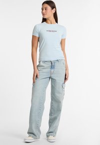 Camiseta ajustada de color azul claro con el logo "GUESS JEANS", combinada con unos pantalones cargo holgados de lavado claro que cuentan con bolsillos laterales y un diseño de pierna recta.