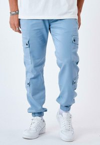 Pantalones cargo azul claros con puños elásticos, múltiples bolsillos laterales con solapas y una textura de tela suave, combinados con zapatillas blancas.