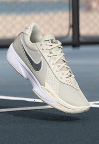 Lys grå atletisk sko med en net-overdel, teksturerede detaljer og en hvid sål. Den har et sølvfarvet Nike-logo og et optimalt stødabsorberende design.