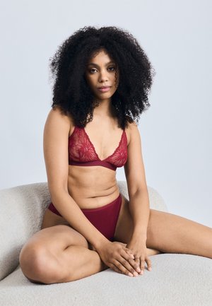 Burgundy-löyhkikankainen bralette kukkakuviolla ja siihen yhdistetyt korkean vyötärön alushousut, jotka esittelevät pehmeää tekstuuria ja herkkiä yksityiskohtia vaalealla taustalla.