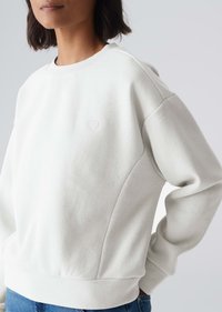 Sweatshirt grigio chiaro con collo e polsini a costine, caratterizzato da un piccolo dettaglio a cuore ricamato sul petto e un design a vestibilità rilassata.
