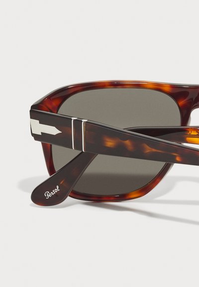 Tortoiseshell sunglasses with dark gray lenses. Features include metal arrow accent, signature logo on the temple, and glossy finish.