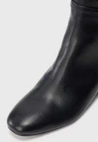 Bota de tornozelo em couro preto com textura suave, bico fino e detalhes de costura discretos ao longo do tornozelo. Design clássico para uso versátil.