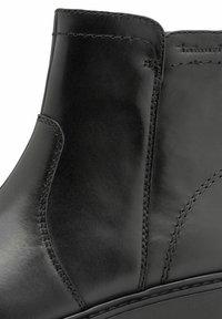 Schwarze Leder-Ankle-Boots mit glatter Textur, geschwungenem Design und verstärkter Naht an den Seiten. Dezentes Branding in der Nähe der Oberkante.
