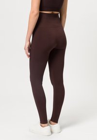 Brązowe legginsy z wysokim stanem wykonane z elastycznego materiału, charakteryzujące się gładką teksturą i dopasowanym krojem, w połączeniu z białymi sneakersami.