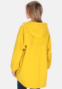 Sárga vízálló dzseki kapucnival, hosszú ujjakkal és laza fazonnal. Rugalmas mandzsettákkal és hátul szellőztető panelekkel ellátva.
