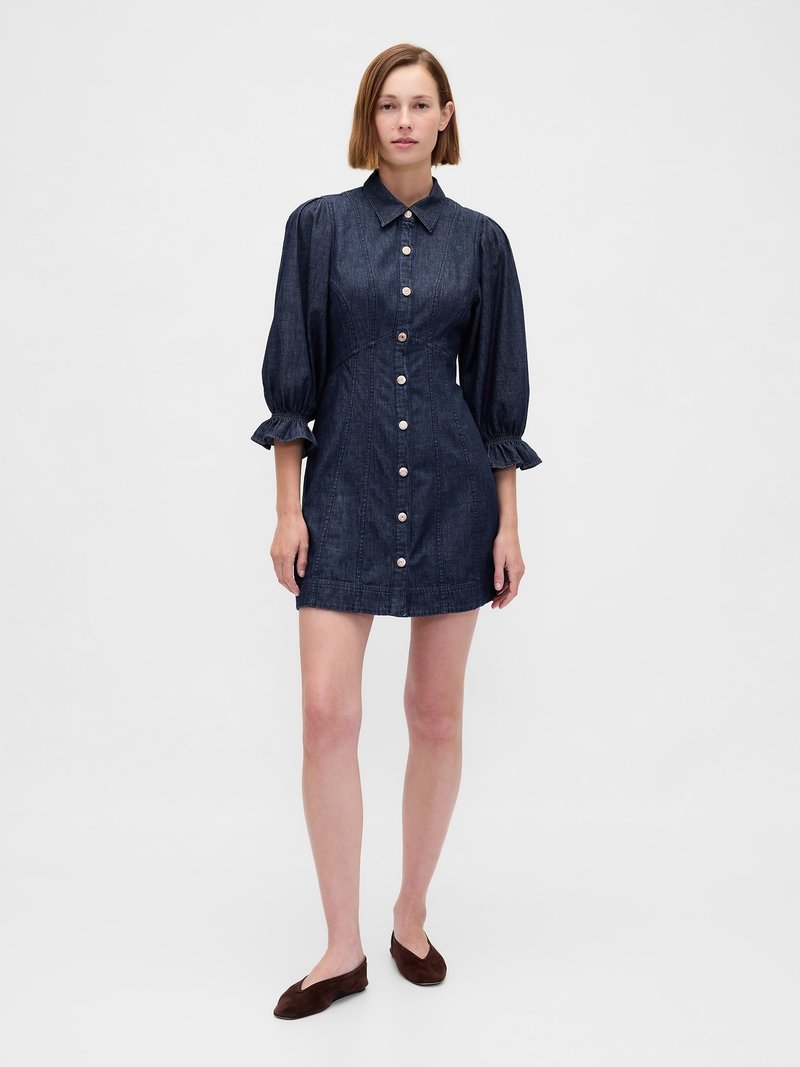 Abito camicia in denim scuro con colletto, maniche a sbuffo e chiusura frontale con bottoni. Presenta polsini arricciati e cuciture verticali.