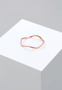 Anello in oro rosa con un design ondulato e aperto. La superficie liscia e lucida mette in evidenza la sua forma organica. Esibito su un pedestal bianco.